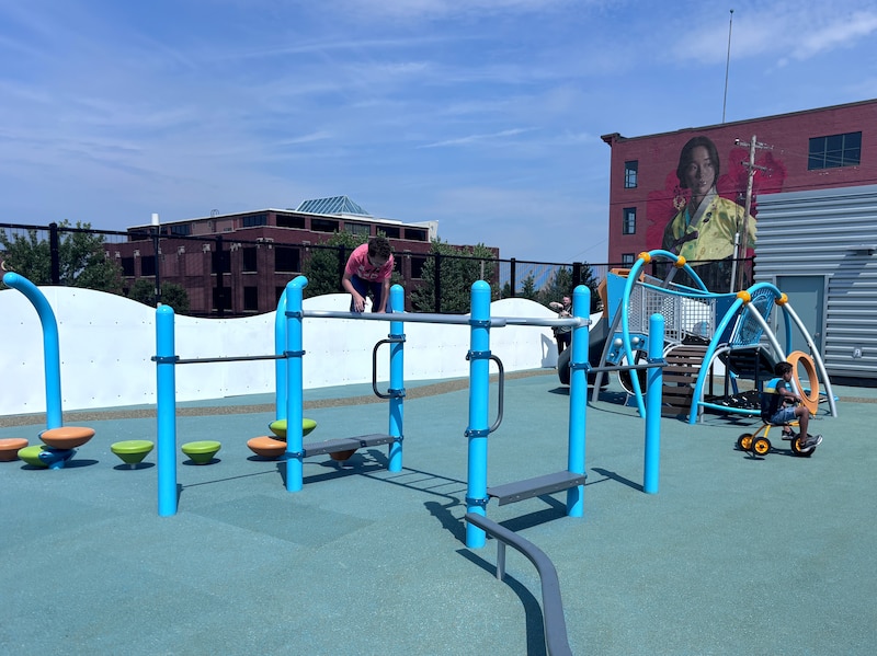 Two young children play on a colorful outdoor playground and there are two buildings in the background.