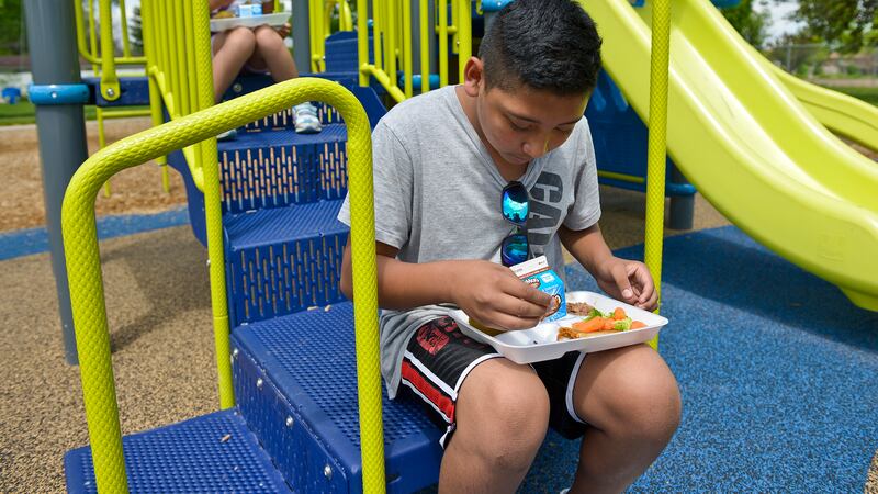 Two young students eat lunch outside on a blue and green playground.