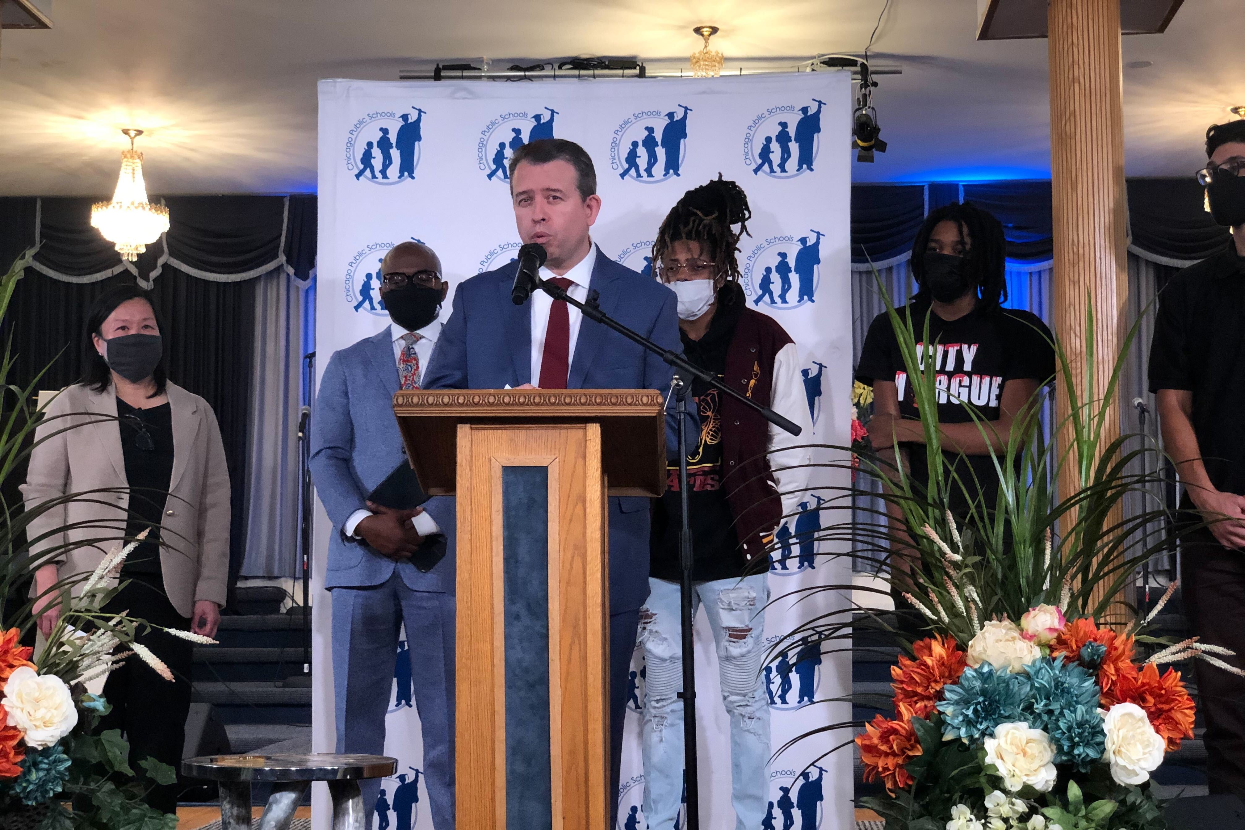 Flanked by district officials and local students, Chicago Public Schools CEO Pedro Martinez stands at a podium in a suit and tie and announces an expansion of a youth violence intervention program Choose for Change.