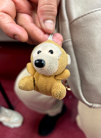 A close up photograph of a hand holding small, tan stuffed animal next to a fanny pack.