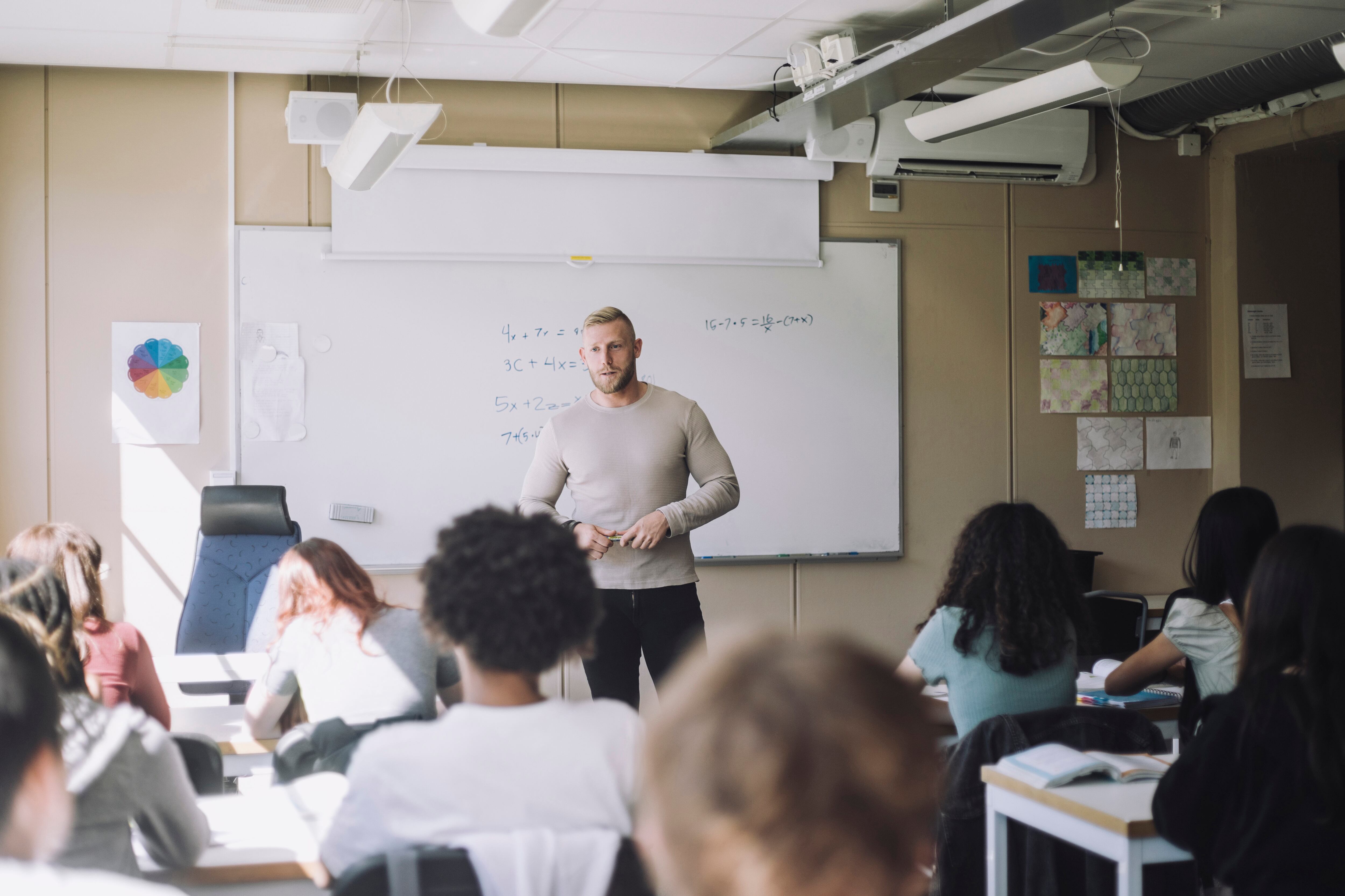 Male teacher stands in front of students in a classroom,