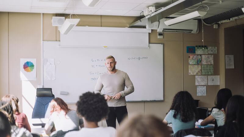 Male teacher stands in front of students in a classroom,