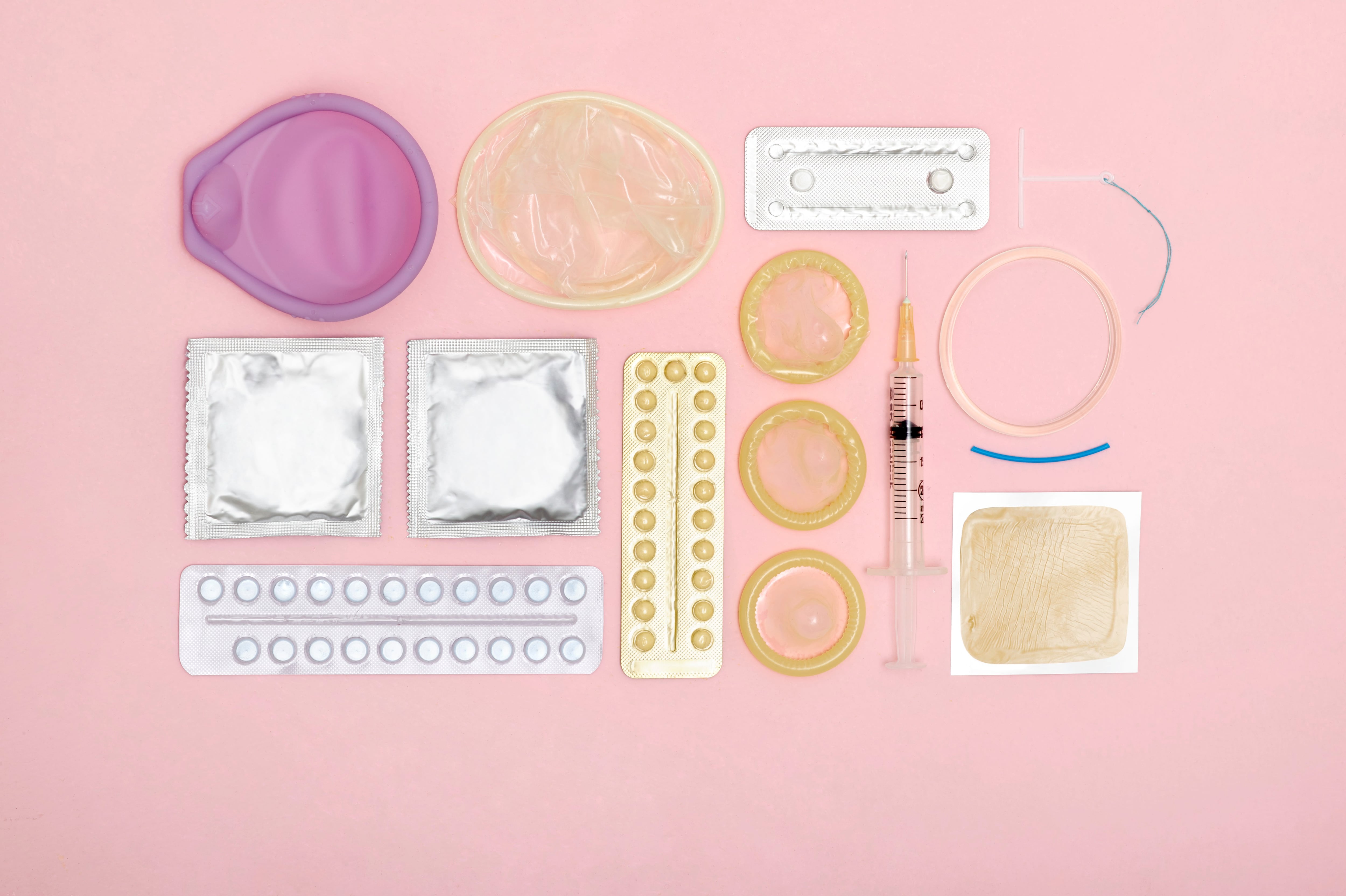 Various contraception items rest against a pink background.