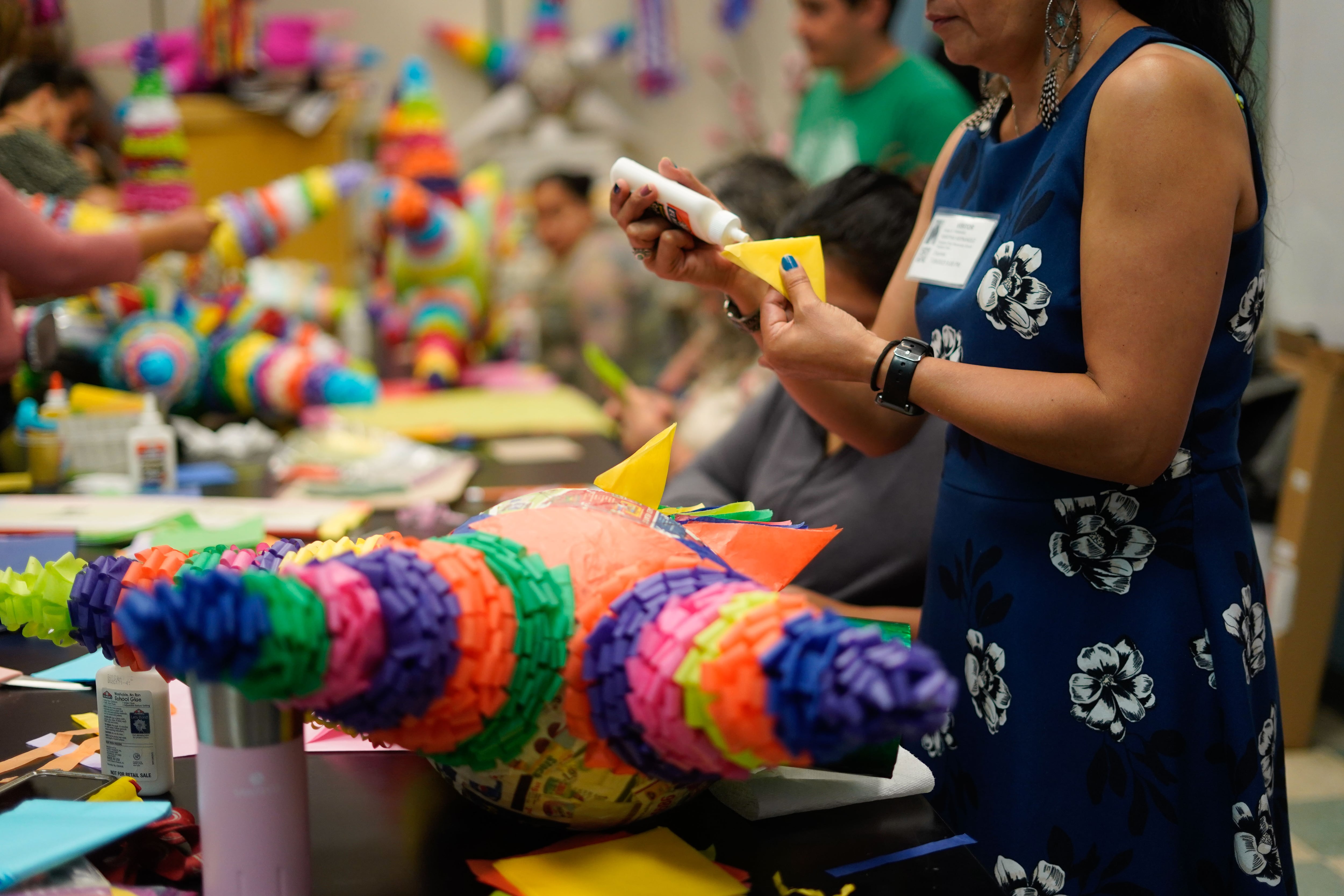 A close up of a colorful piñata in the shape of a star and a woman's pair of hands attaching piece of colorful paper with glue.