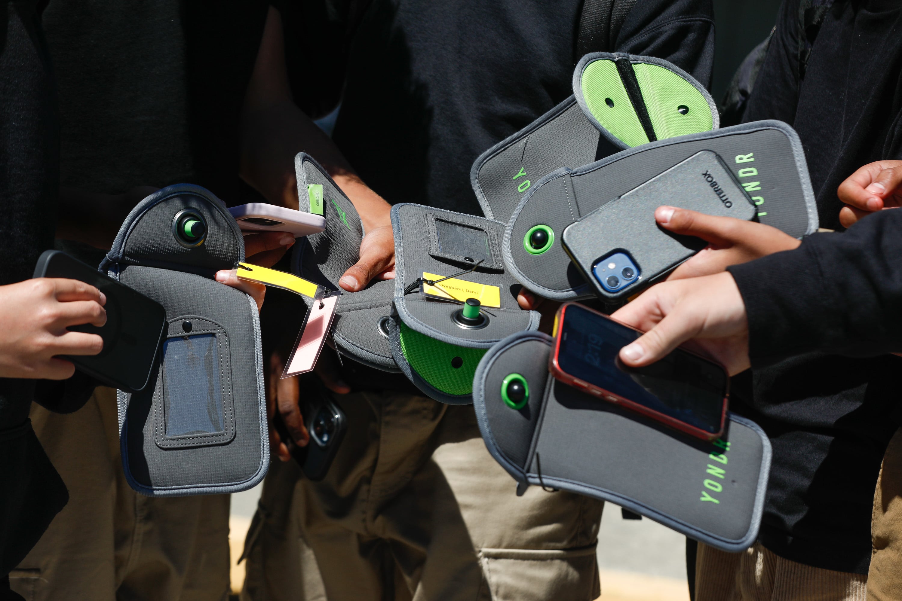 A group of hands holding cellphones and security pouches.