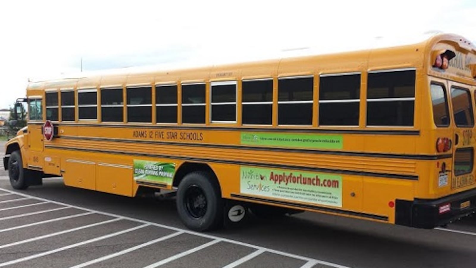 An Adams 12 school bus with an advertisement for the online application for free and reduced-price meals.