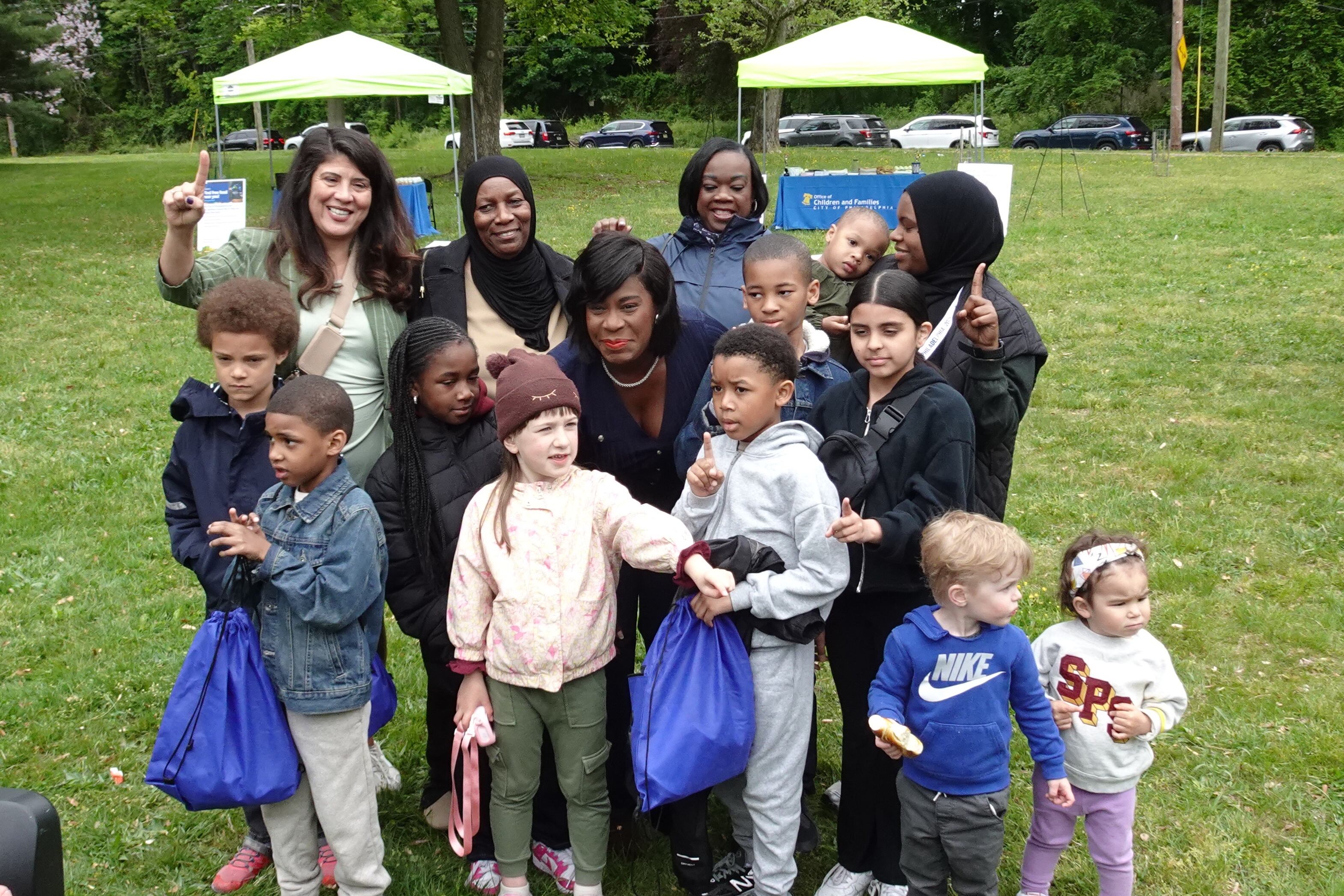 Philadelphia Mayor Cherelle Parker smiles surrounded by a group of young kids and parents in the rain in a park.