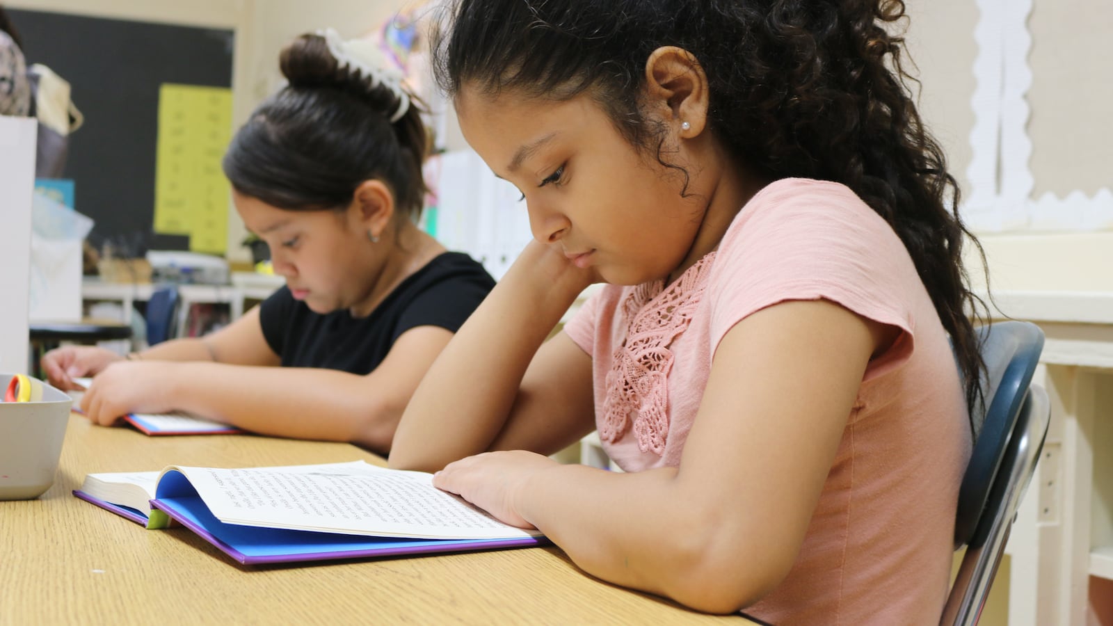Two students read at a table in a classroom.