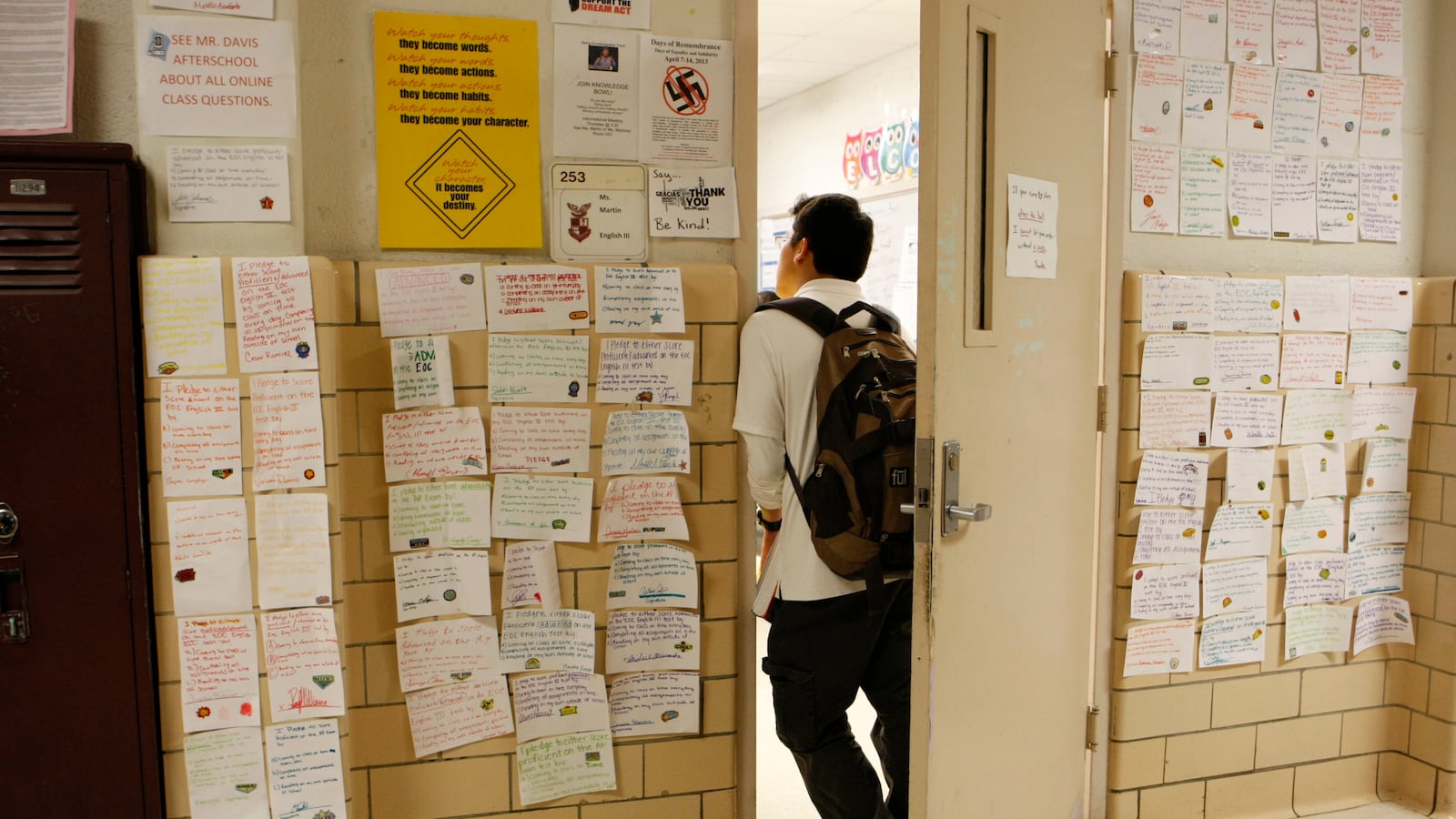 A teenage male student wearing a white shirt, dark pants, and a backpack stands in the doorway of Kingsbury High School in Memphis.