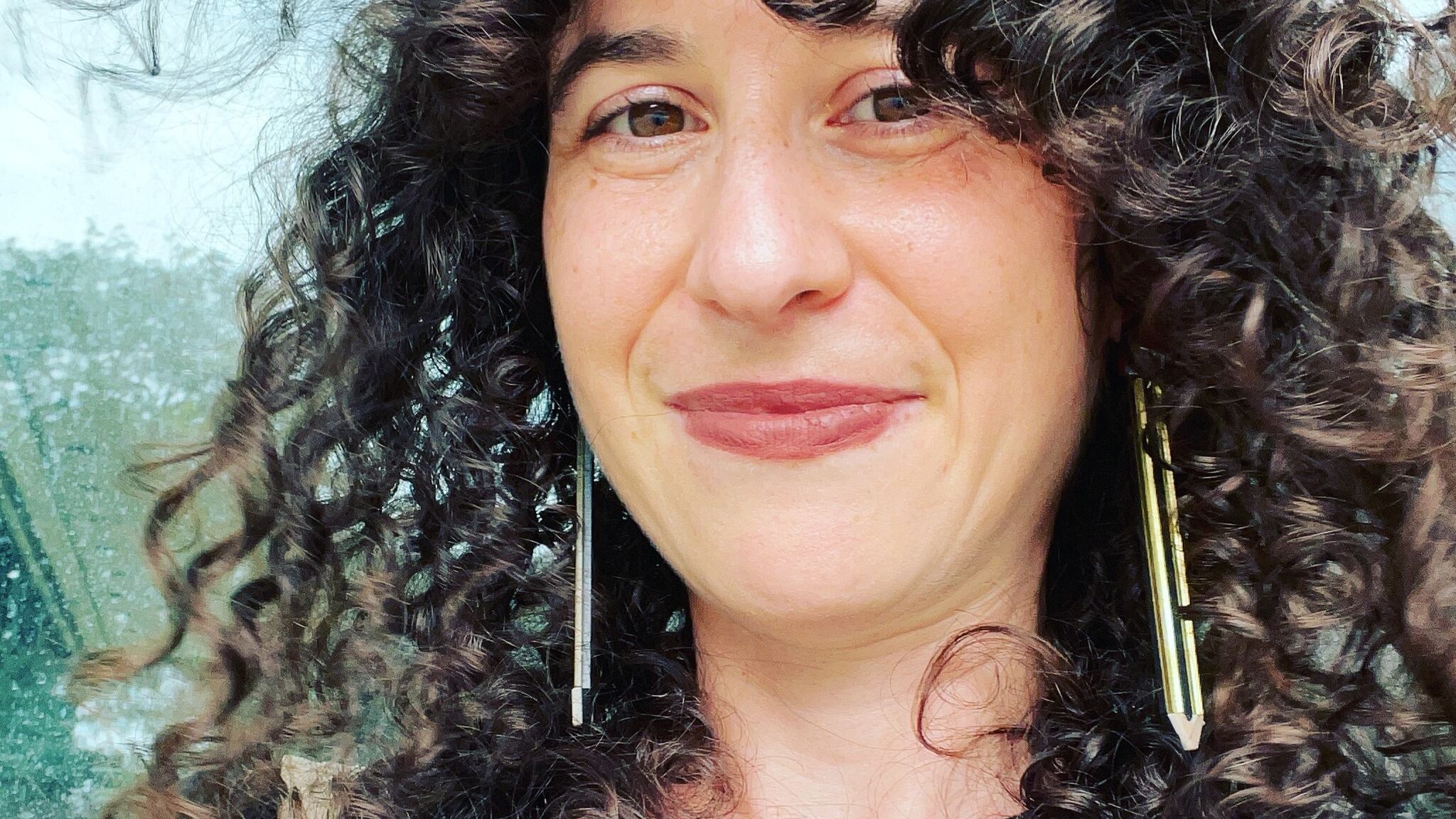 A white woman with curly hair smiles at the camera.