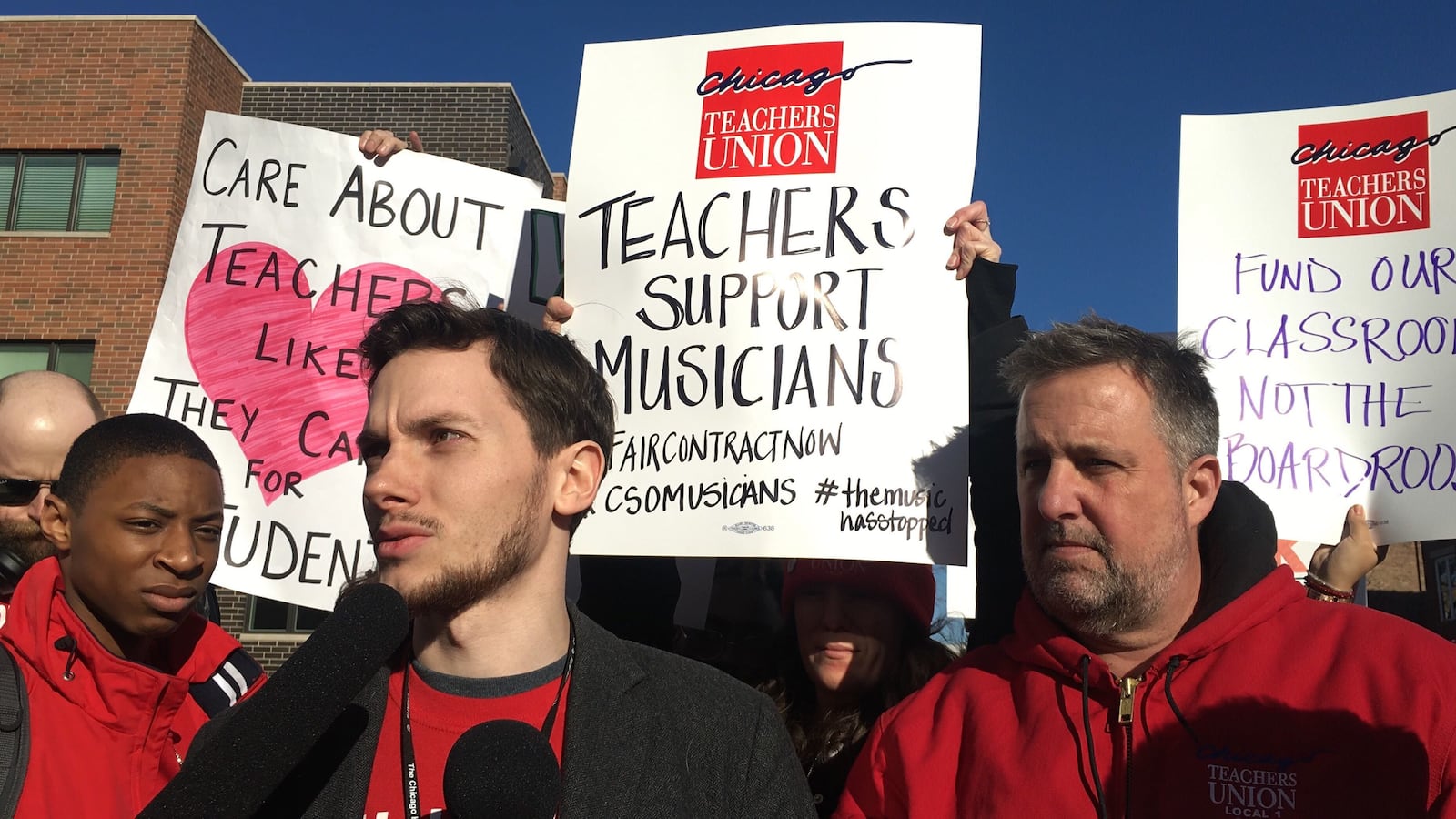 Teacher Andrew Van Herik, center, with microphone, and Chicago Teachers Union charter division President Chris Baehrend speak at a press conference outside the Chicago High School of the Arts.