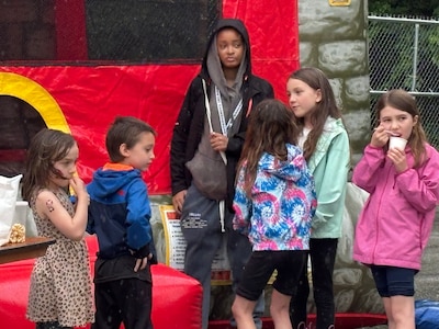 A group of six young students stand outside of a bouncy house.