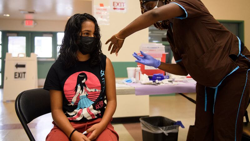 A young woman wearing a black and red japanese art-inspired shirt receives a dose of the COVID vaccine from a nurse.