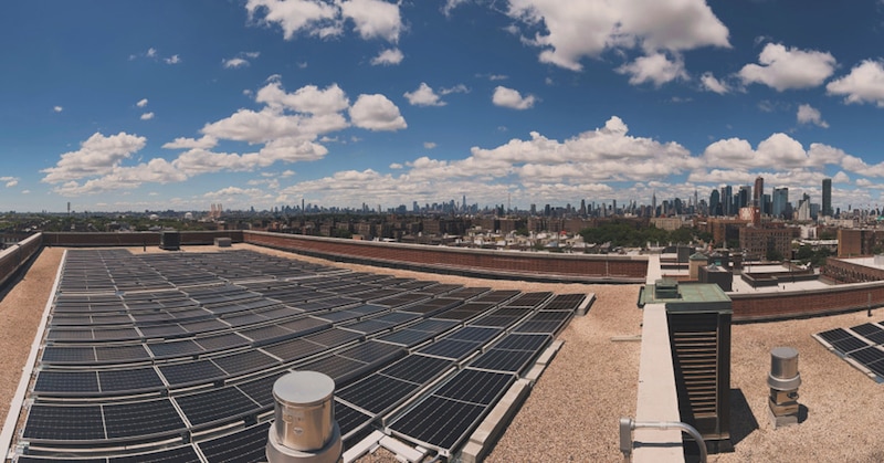 A photograph of a strip of solar panels on the roof of a buildings with the NYC skyline in the background.
