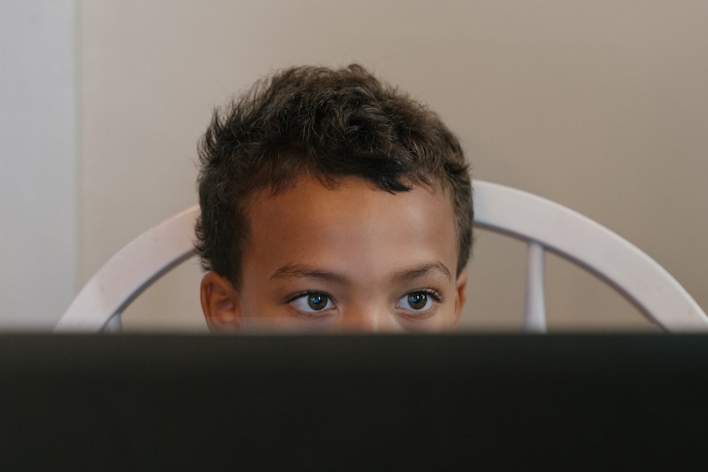 A young boy's eyes peer above a computer.