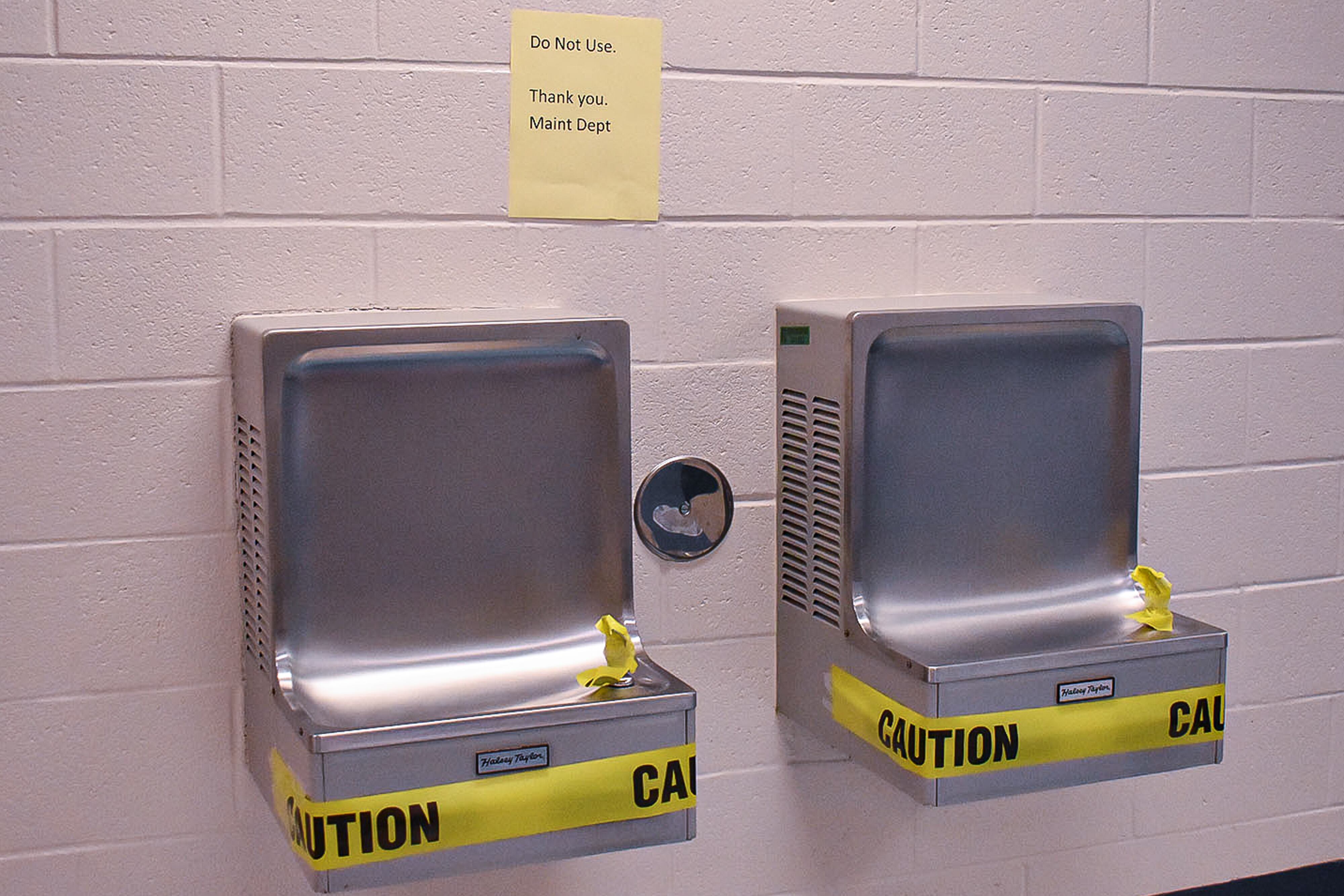 Two wall-mounted water fountains are marked with caution tape to prevent use.