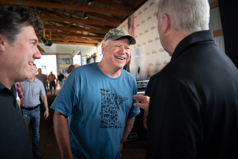 A man wearing a blue t-shirt and a baseball cap stands between two people.