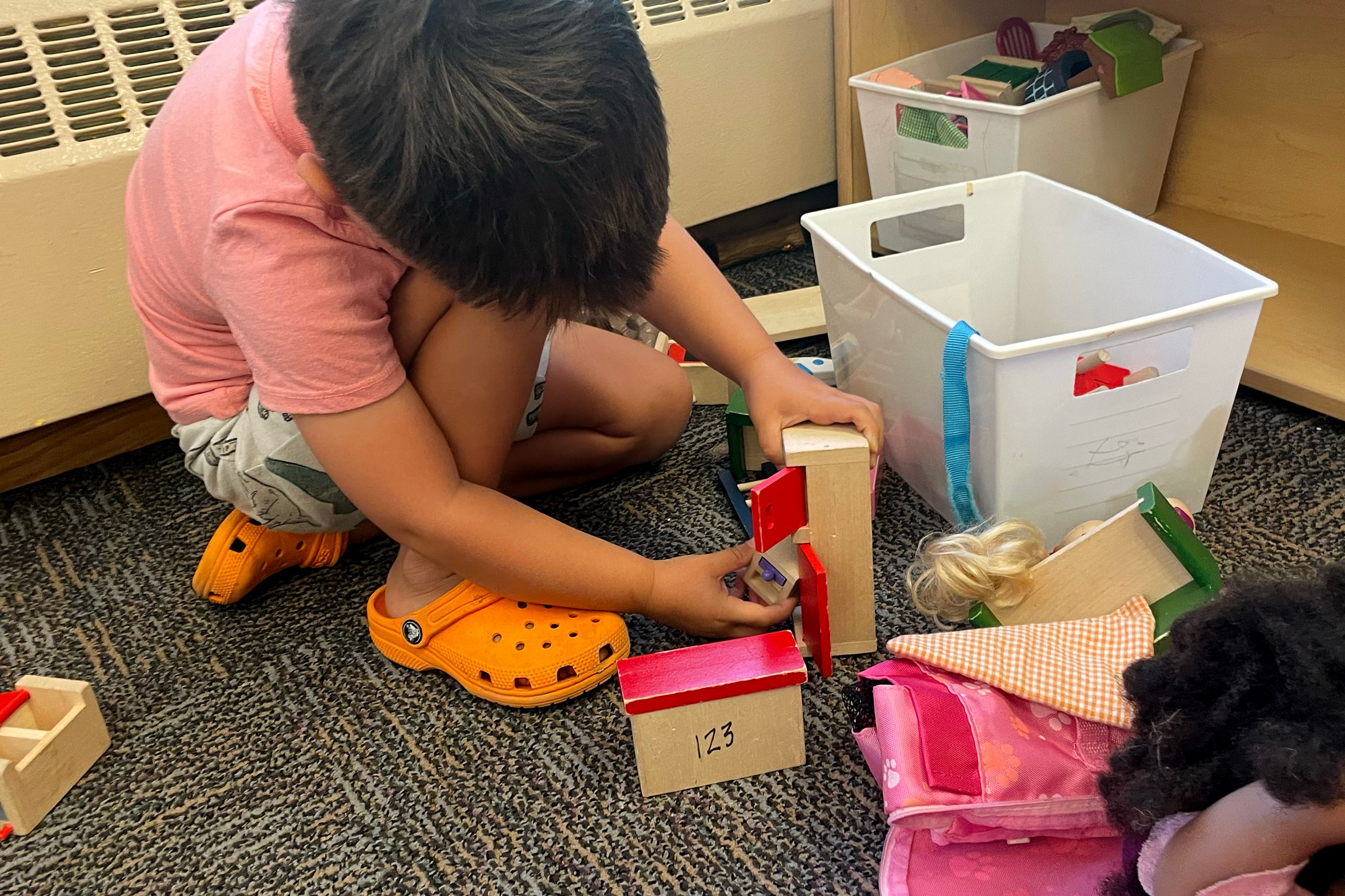 A young boy in a pink shirt plays with small toys on the floor.