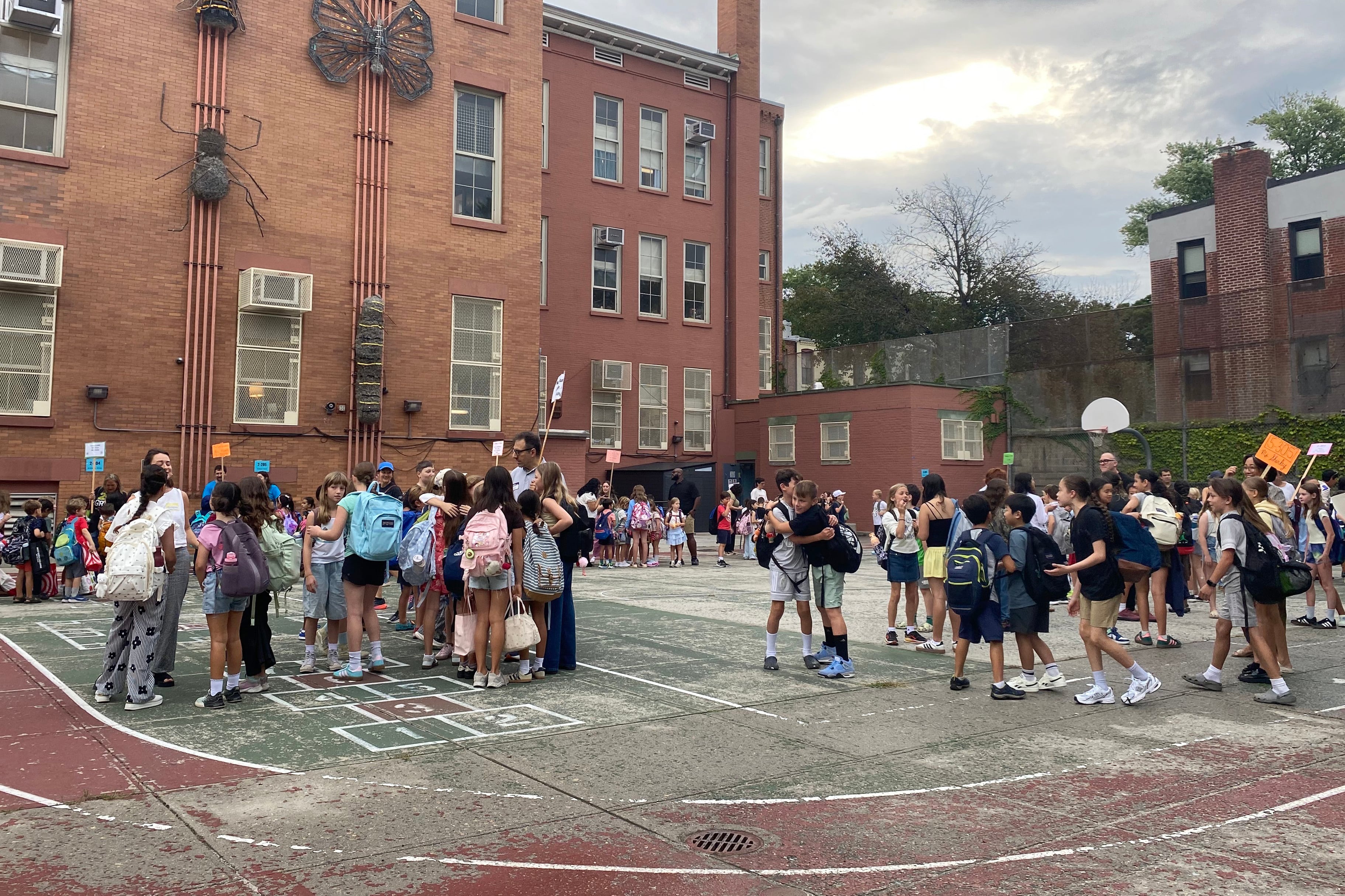 Students wait outside of a school building on a playground on a cloudy day.