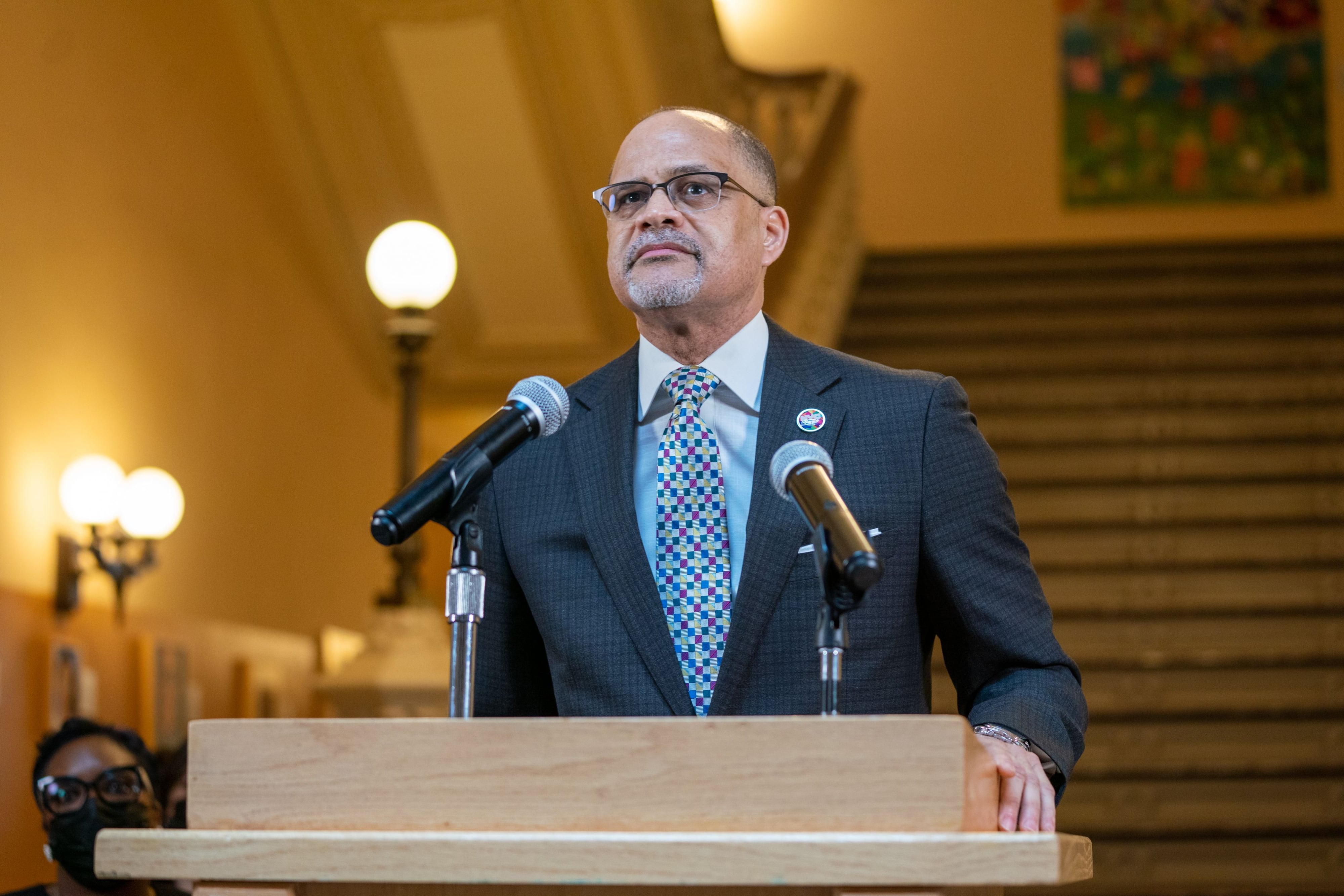 A man in a suit stands at a lectern.