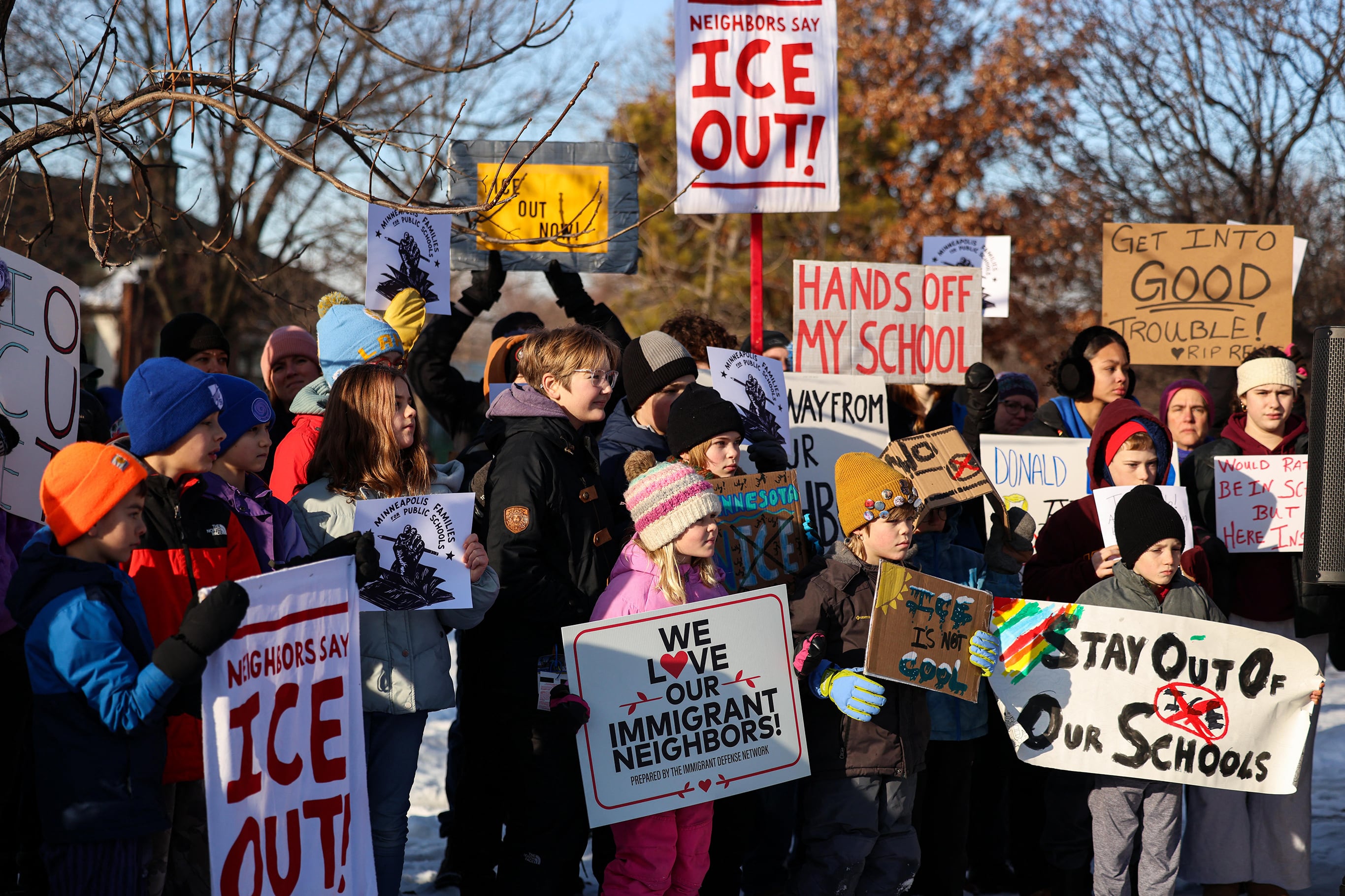 A photograph of a large protest of adults and a lot of children bundled up in large winter coats and hats and holding signs demanding ICE out of schools, communities, etc.
