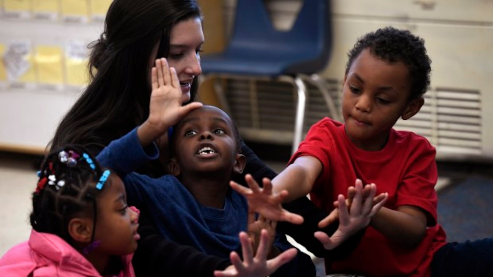 Paraprofessional Madison Marasco counts to 10 with kindergarten students Salah Osman, Za'Mayah Jones, and Deangelio Heard at Denver's Fairview Elementary.