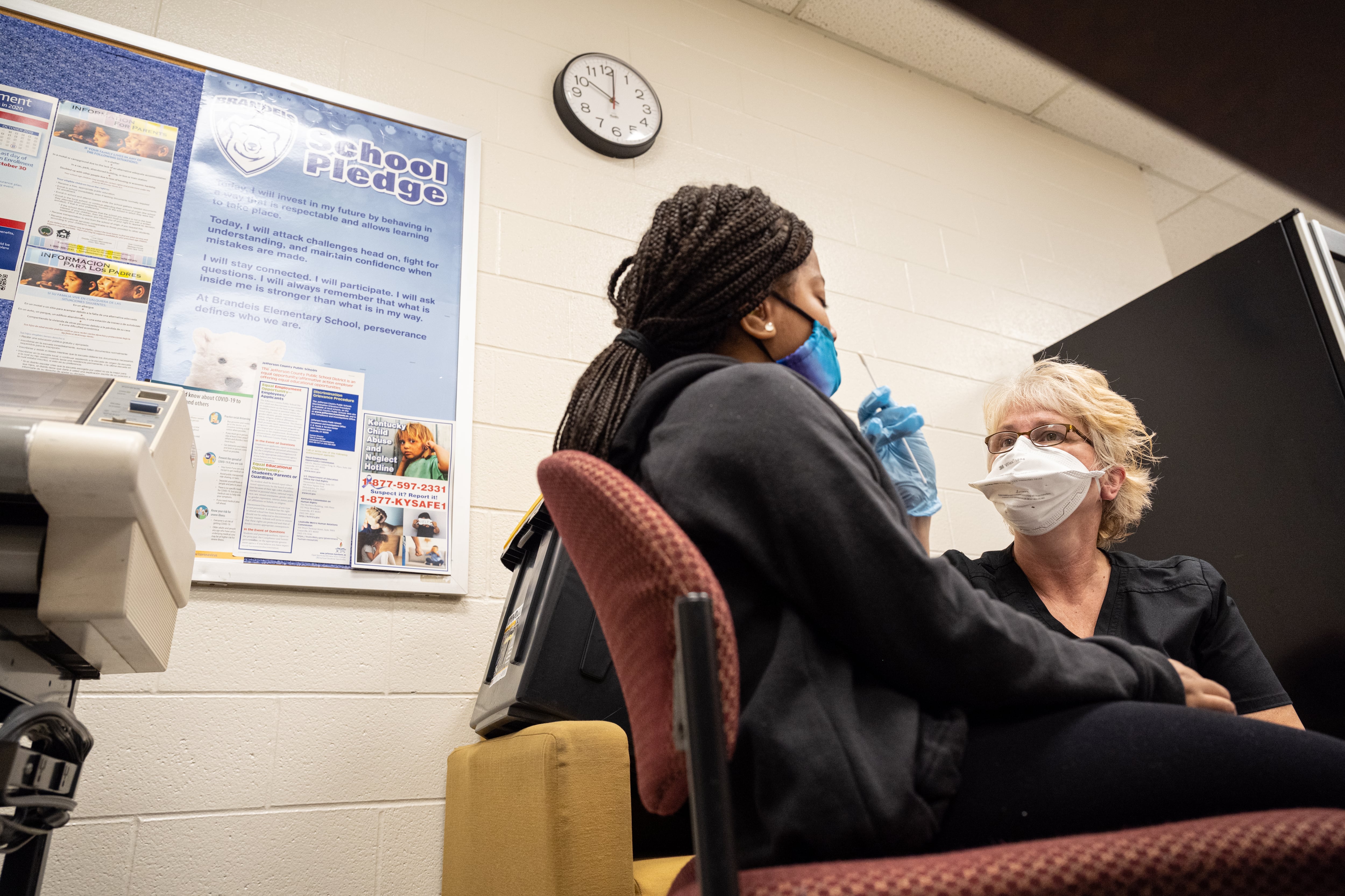 A student with long braided hair is tested for COVID by a nurse wearing black scrubs.