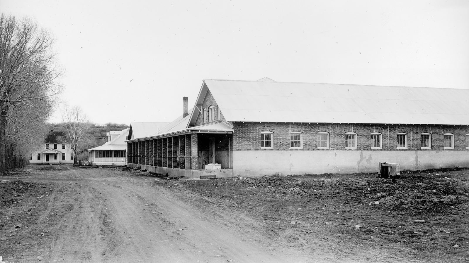 A black and white photograph of a building next to a dirt road. 