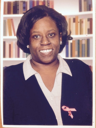 A photograph of a Black woman posing for a picture in front of a colorful background.