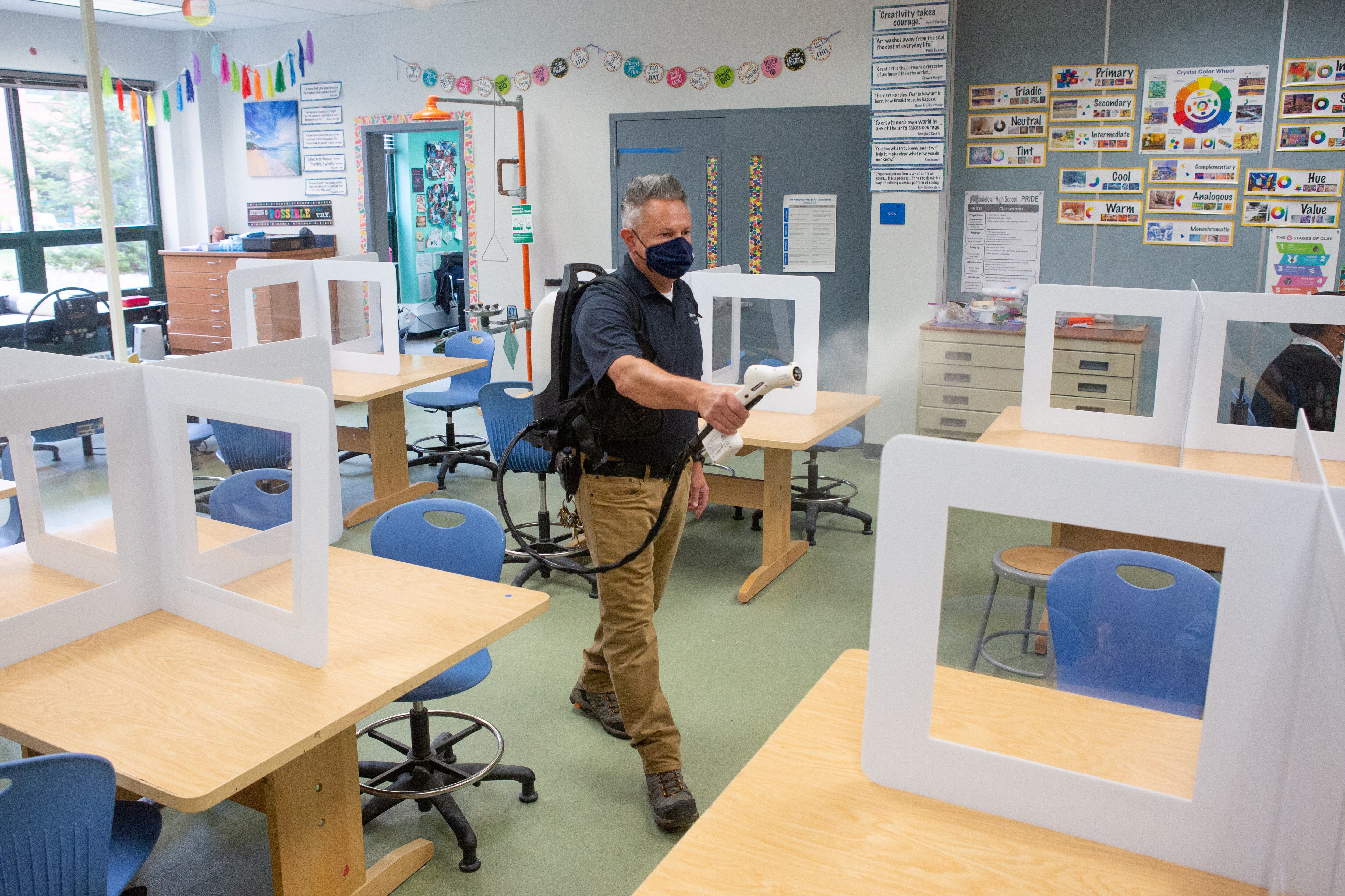 Janitorial staff member Jeffrey Turro uses a disinfectant spray gun to clean a classroom.