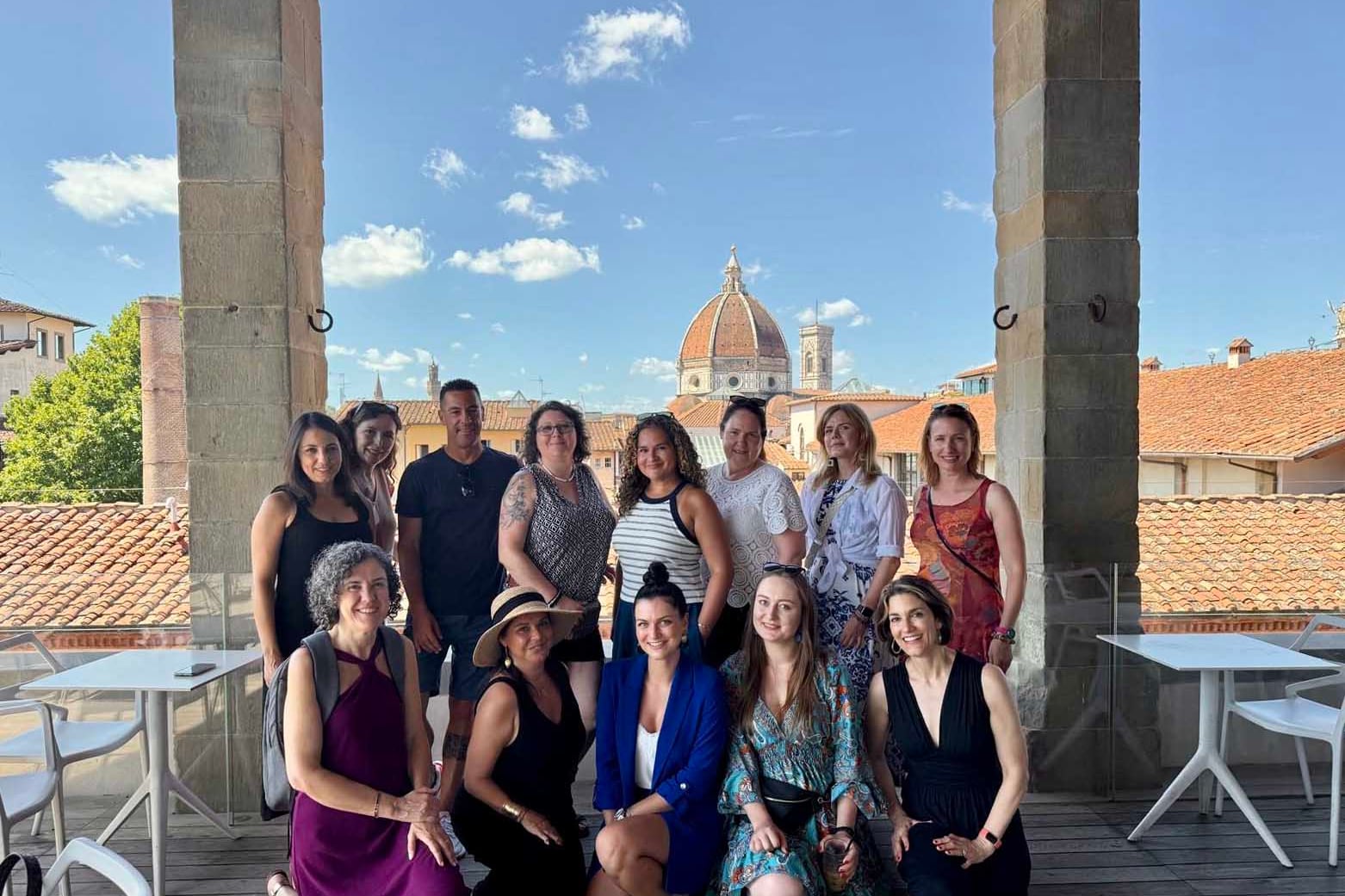 A photograph of a group of adtuls in two rows posing for a photograph in Italy.