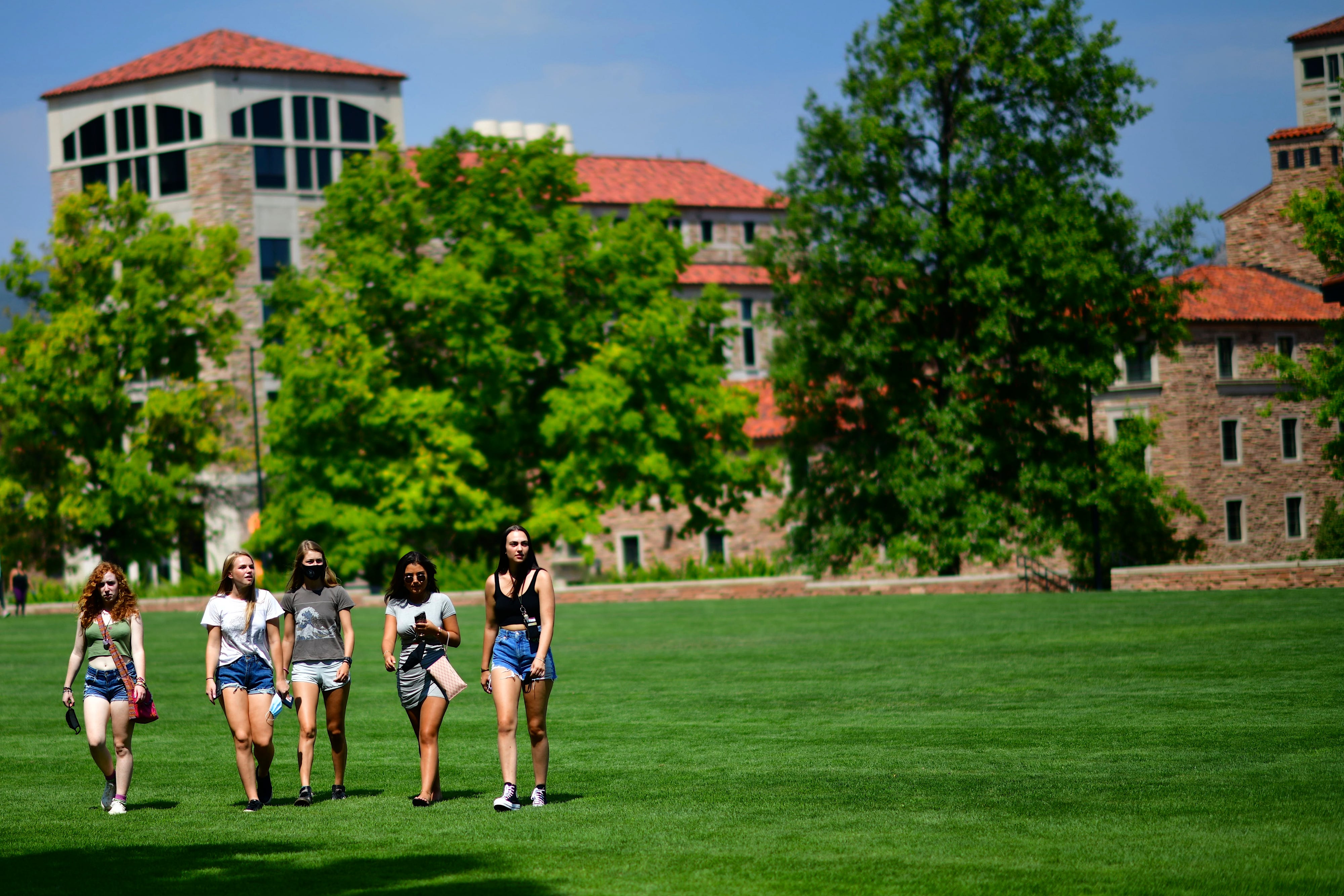 A group of five young women walk across a large field on the campus of Colorado University.