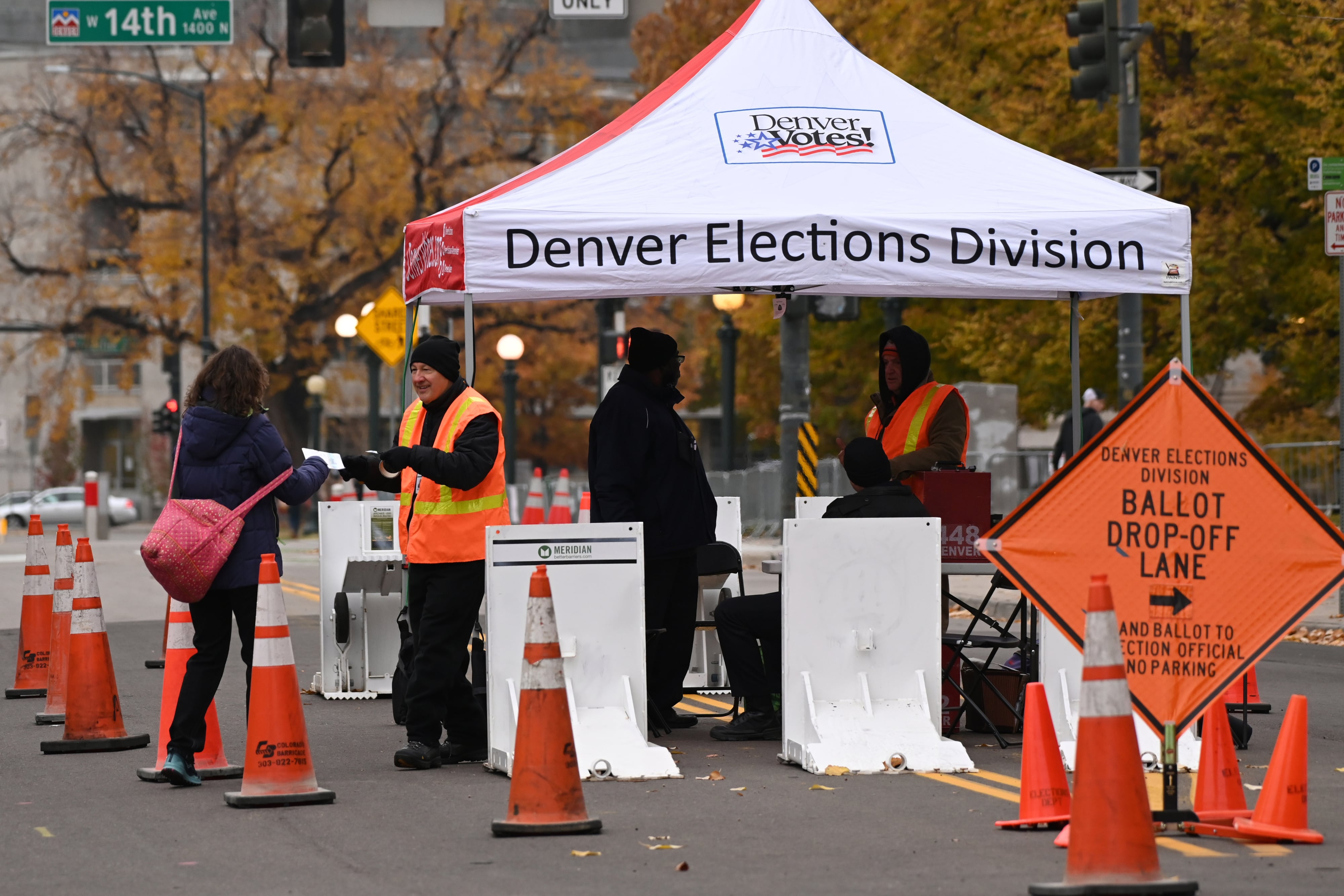 Poll workers gather ballots at a Denver Elections Division polling site, marked off by a series of orange traffic cones.