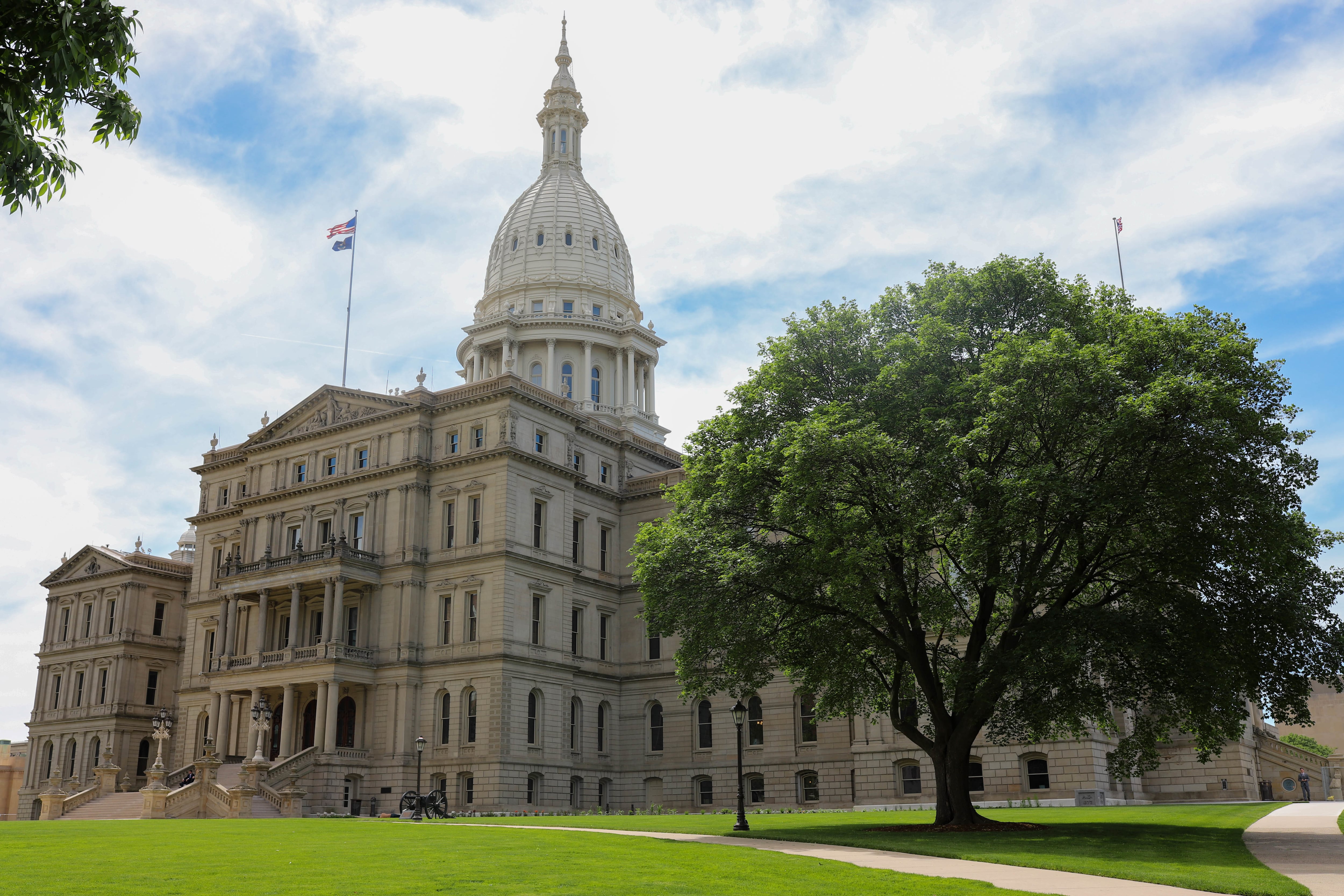 A large white stone Capitol building with a blue sky and large green trees.