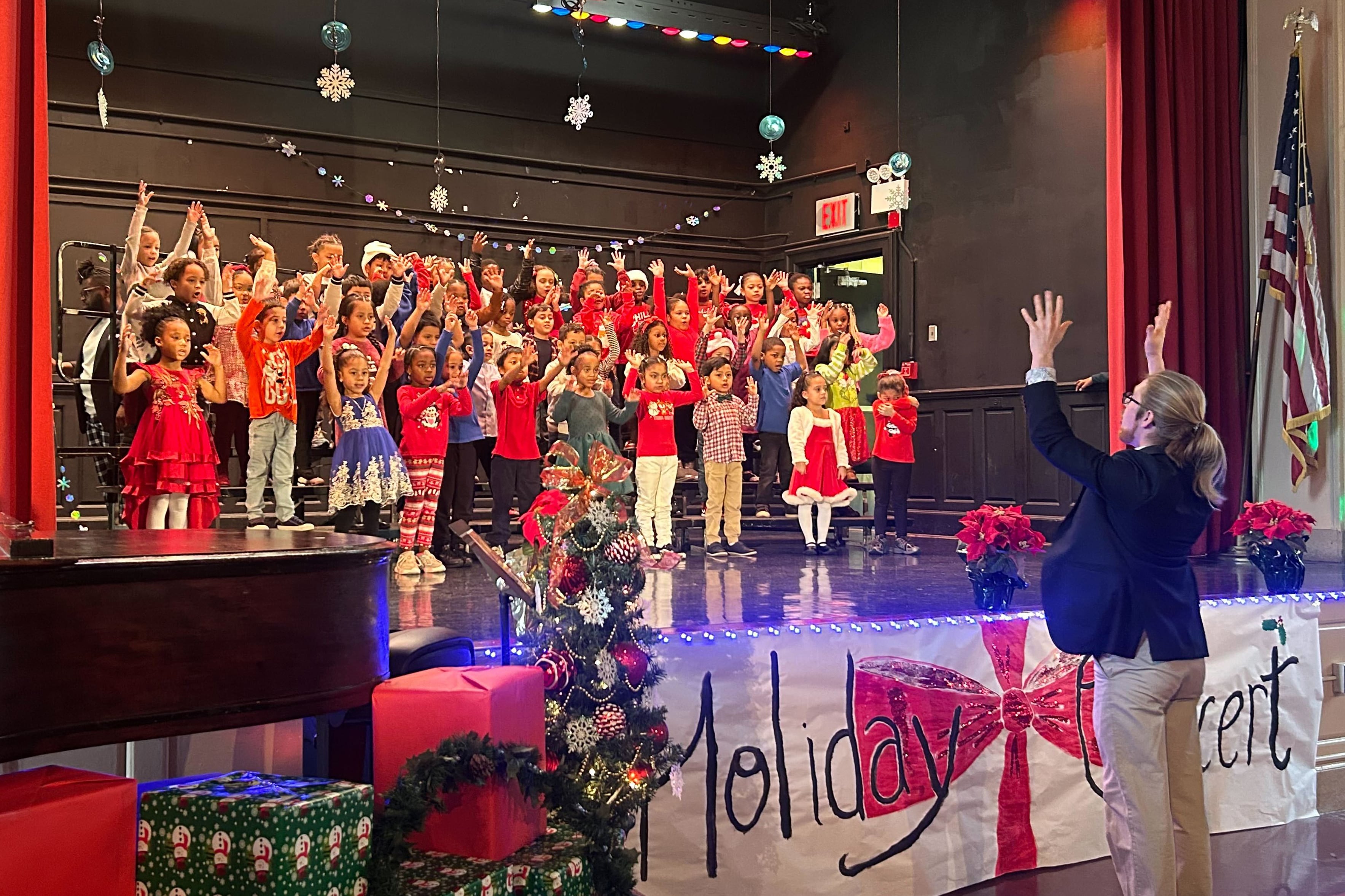 A group of students perform on stage while an adult composes in the foreground.