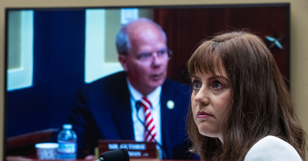 Two people seated at a hearing table, shown on a video screen