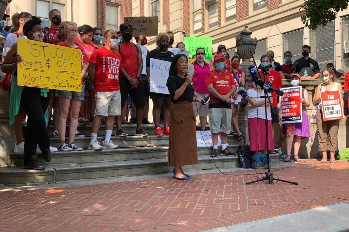Councilwoman Helen Gym speaks outside Masterman High School with a microphone. A group of protesters stands around her, some holding signs.