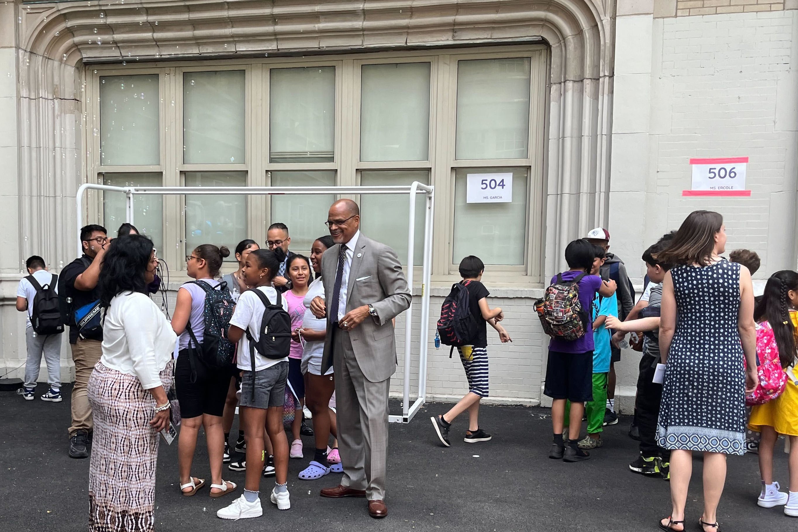 A group of adults and students say goodbye outside of a school on the last day of school.