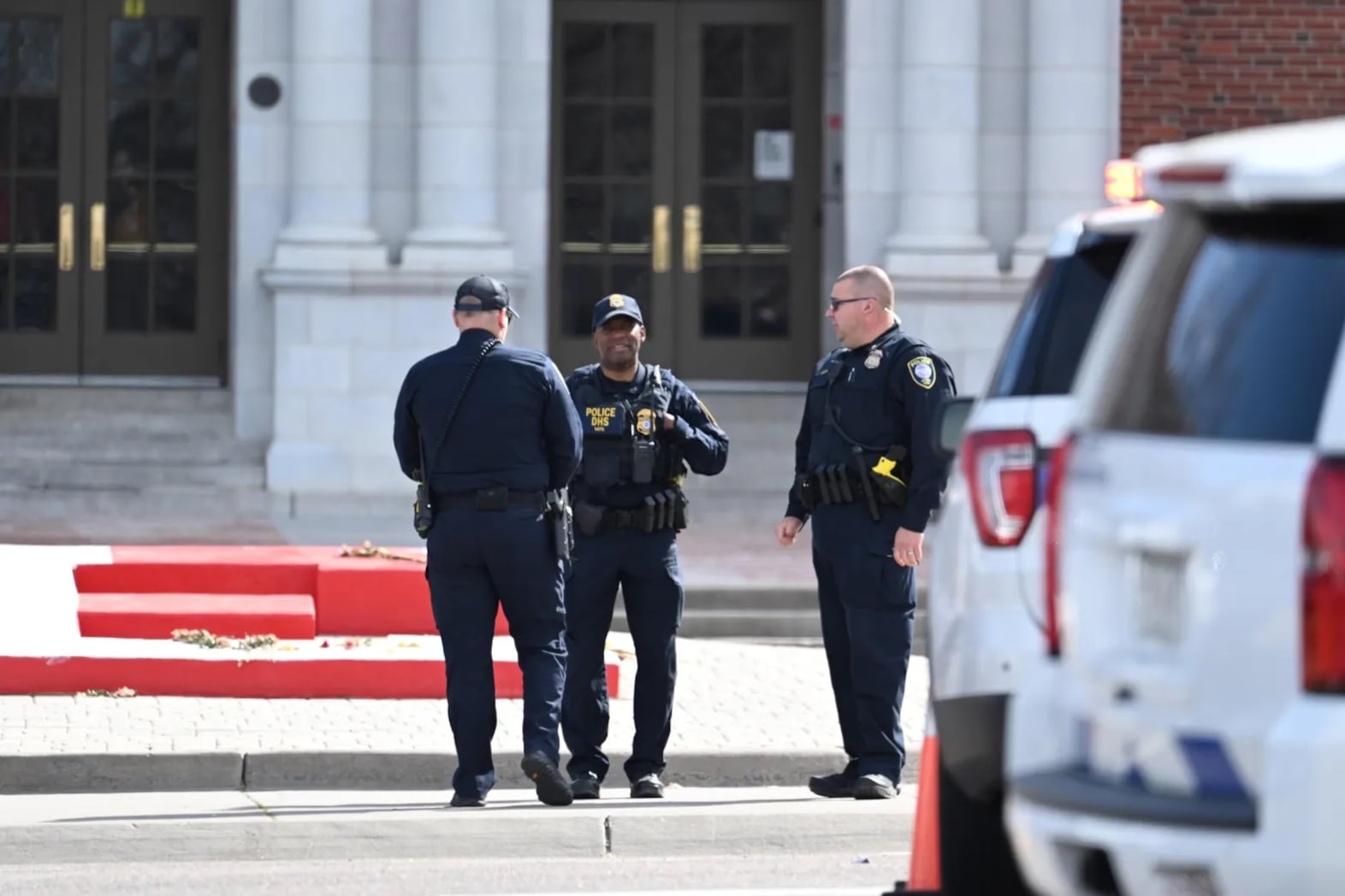 Three police officers stand in front of steps of East High School in Denver, Colorado, after a shooting there on March 22, 2023.
