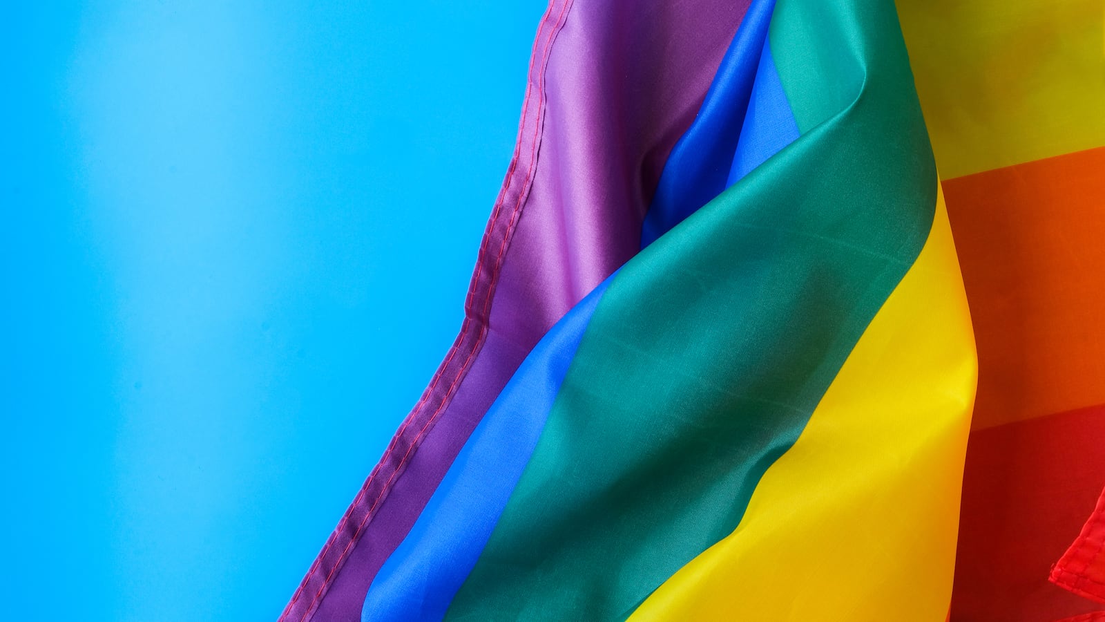 A rainbow flag against a blue sky.