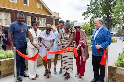 A photograph of a line of adults cutting a red ribbon outside.