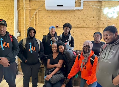 A group of students and a teacher pose for a photograph in a room with a yellow wall in the background.