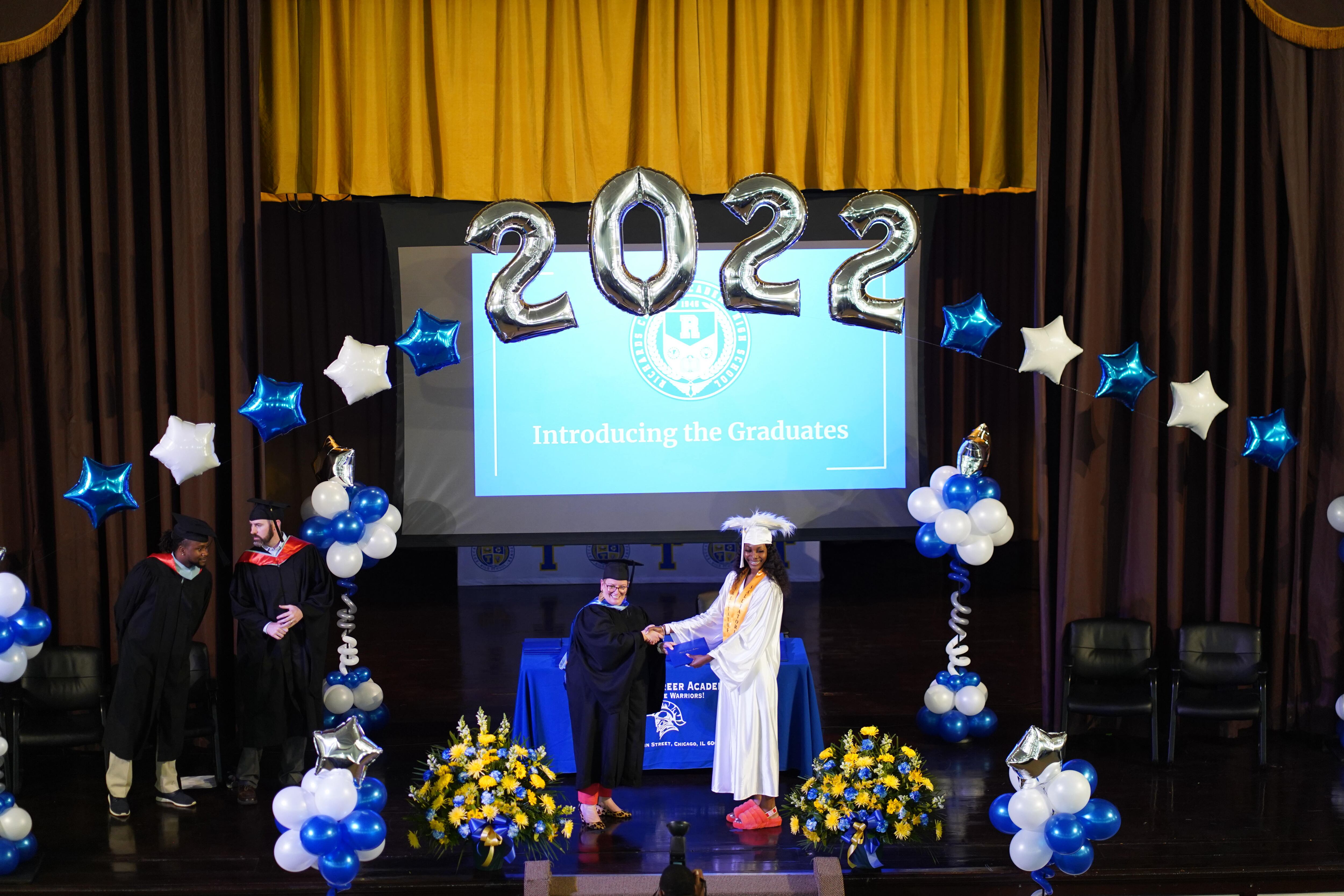A student shakes hand and accepts her high school diploma from a school administrator.