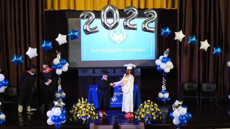 A student shakes hand and accepts her high school diploma from a school administrator.