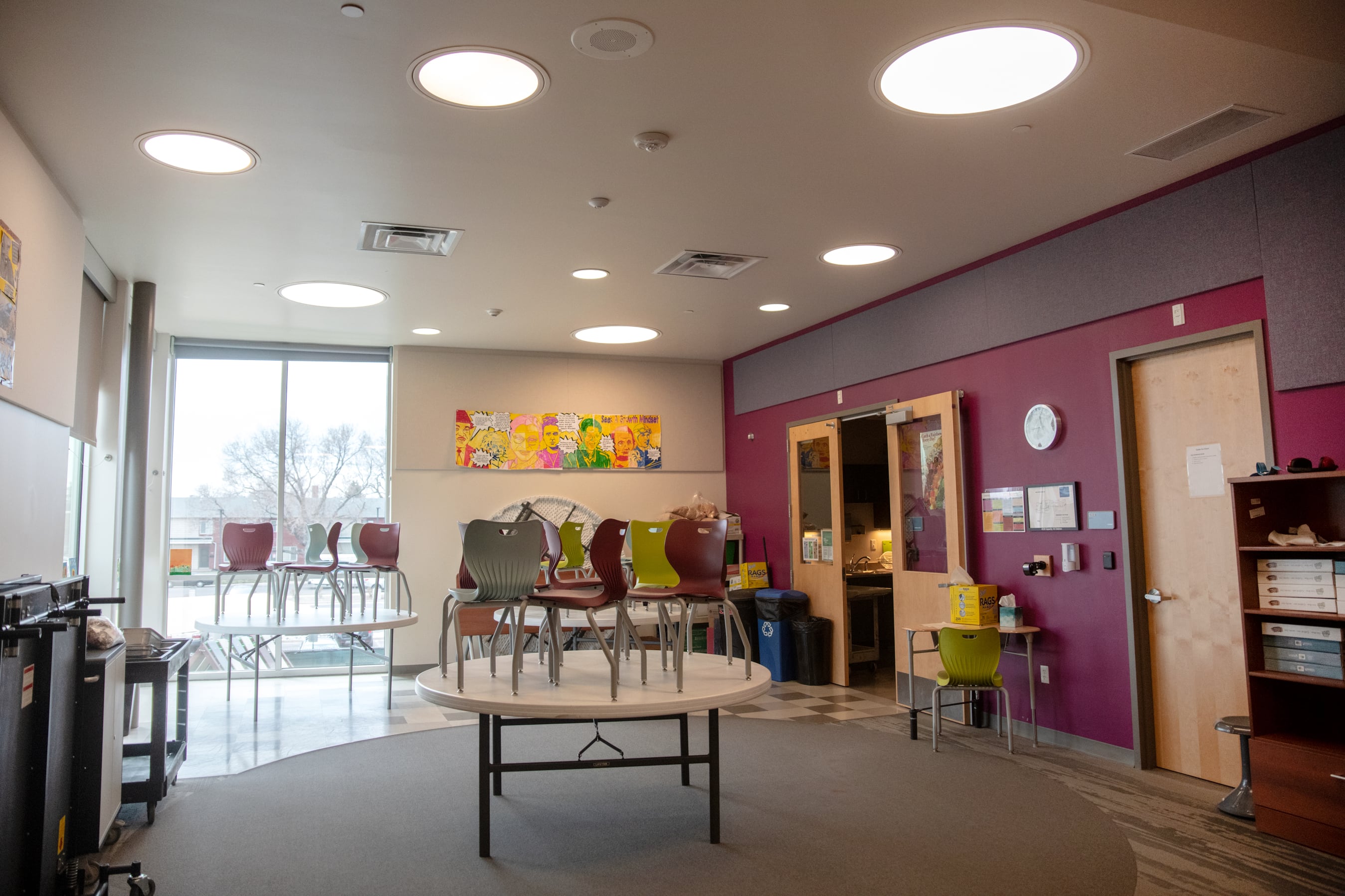 Chairs are stacked on tables in a colorful classroom in hues of purple and green.