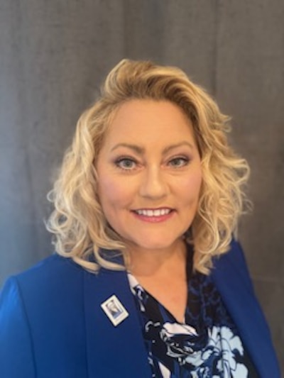 Portrait of Kimberly Huffman. She is wearing a blue blazer and a patterned blouse. She has shoulder-length blond hair. She is smiling at the camera.