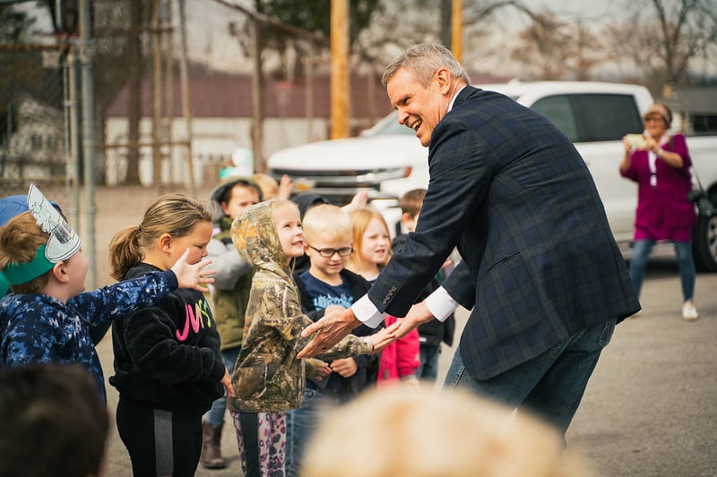 A man greets children outside of their school