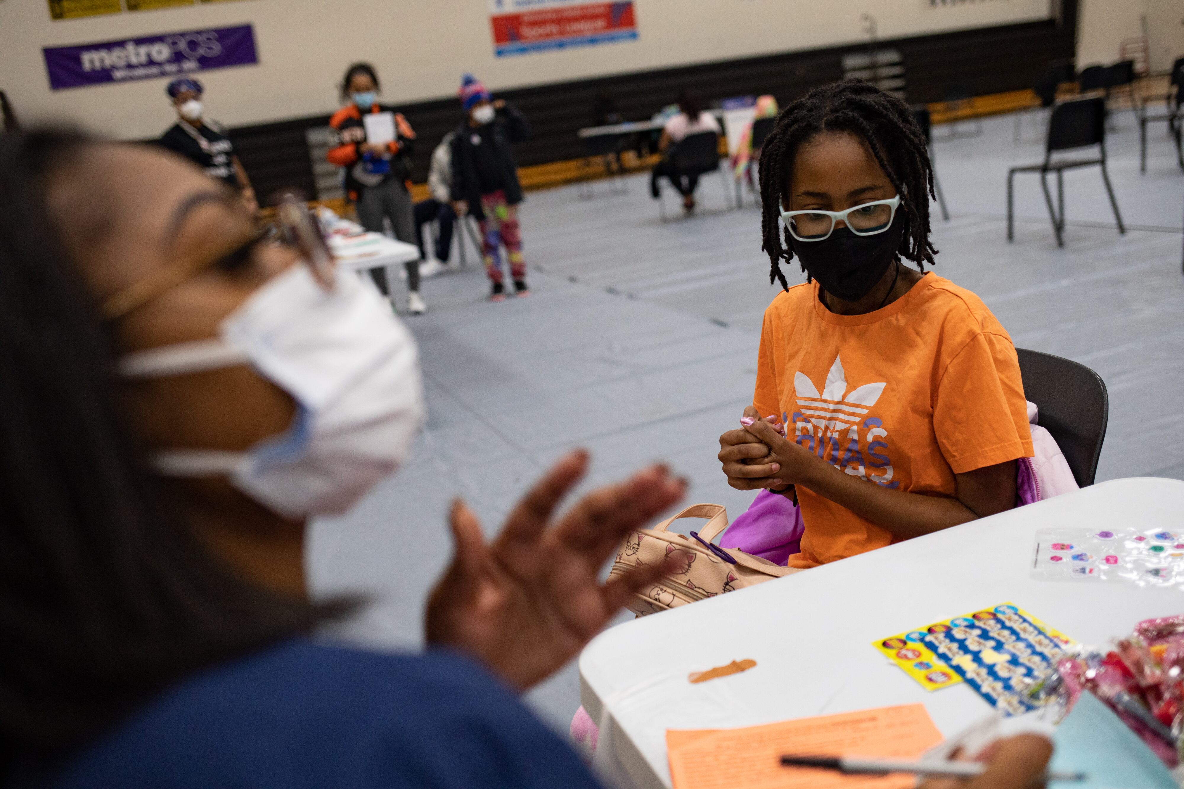 A girl sits waiting in an auditorium alongside a health worker for her first COVID-19 vaccine.