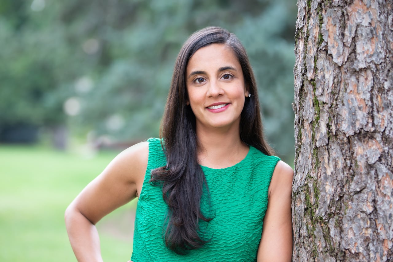 A woman in a green top leans against a tree.
