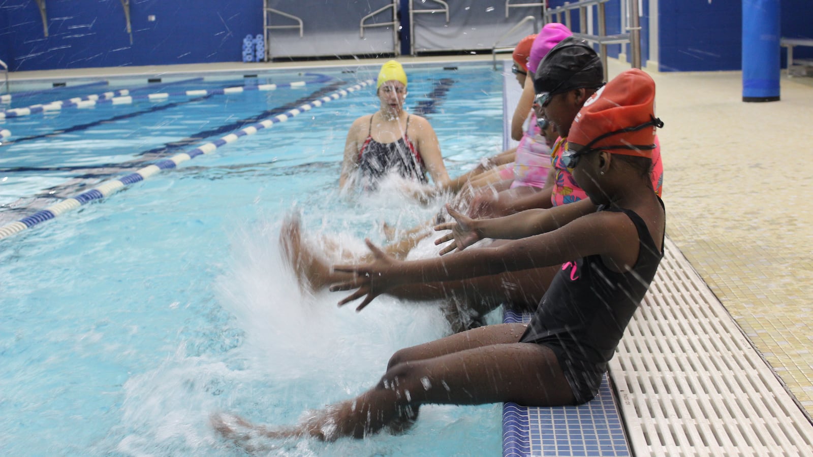 About half a dozen students try flutter kicks in a pool while an instructor watches nearby.